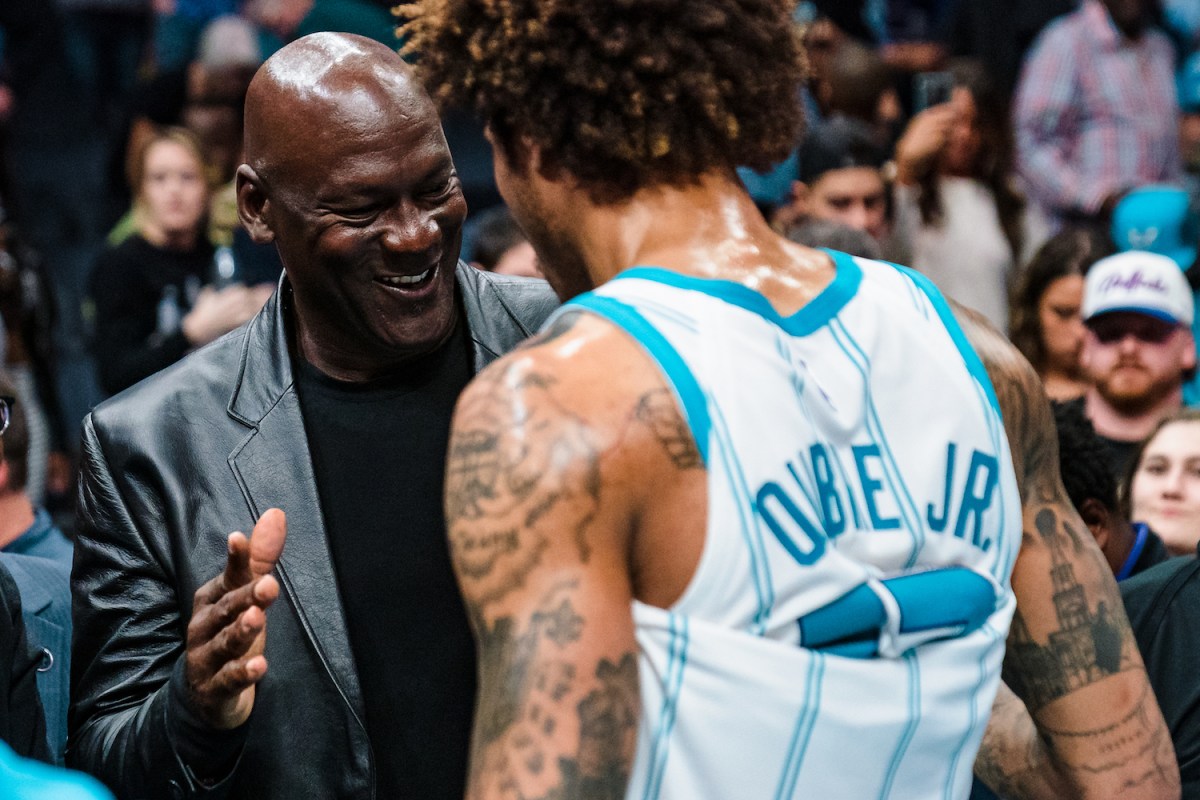 Michael Jordan, owner of the Charlotte Hornets, goes in for a handshake with one of his team's players on the sidelines of a basketball court