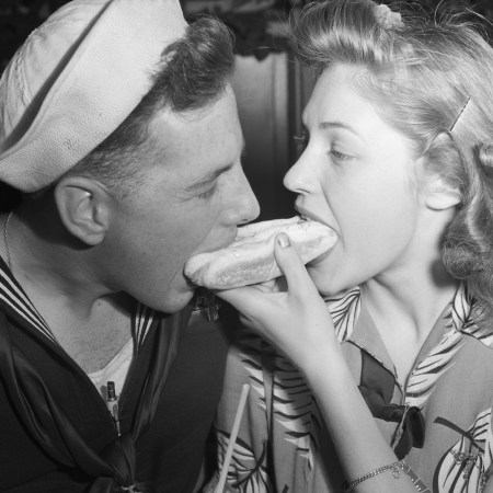 woman and her sailor boyfriend eat from both ends of a hot dog