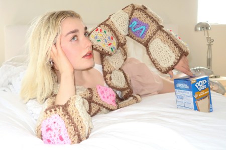 A woman wearing the Pop-Tarts Pop-Tartigan sitting next to a box of the new Frosted Banana Bread flavor