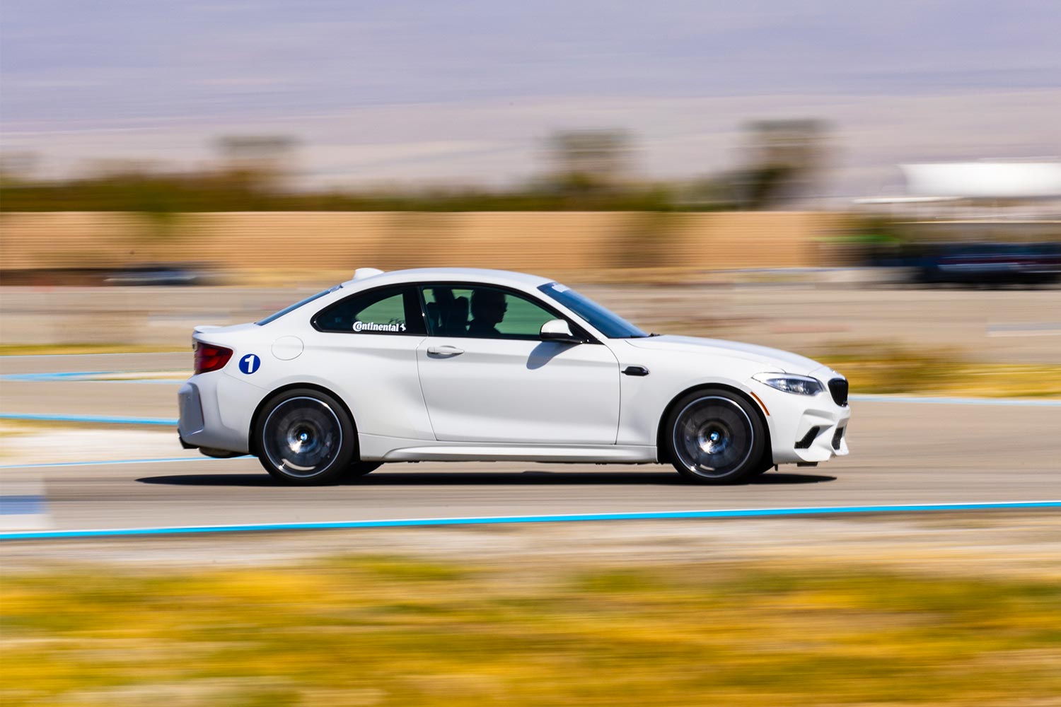 A white BMW M model speeding down the track at the BMW Performance Driving School in California