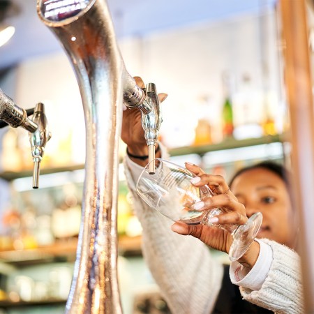 Close-up of a African American bartender woman pouring a glass of tap beer in a bar.