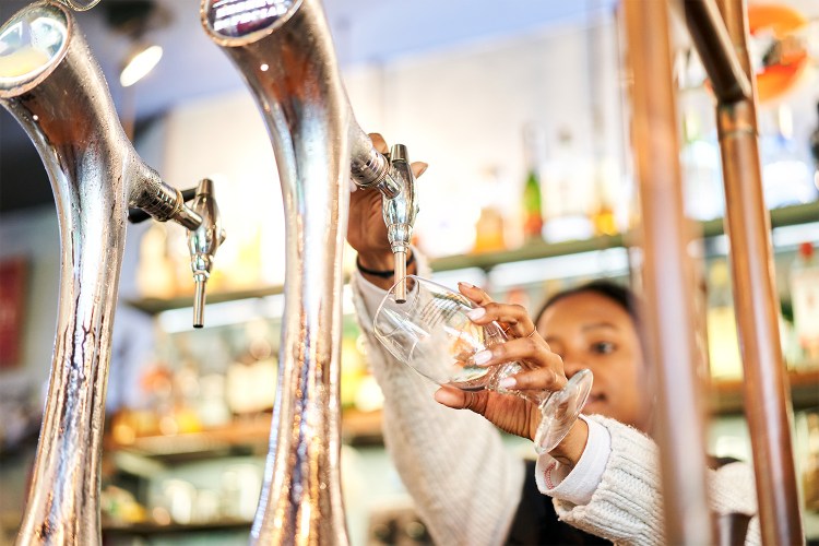 Close-up of a African American bartender woman pouring a glass of tap beer in a bar.