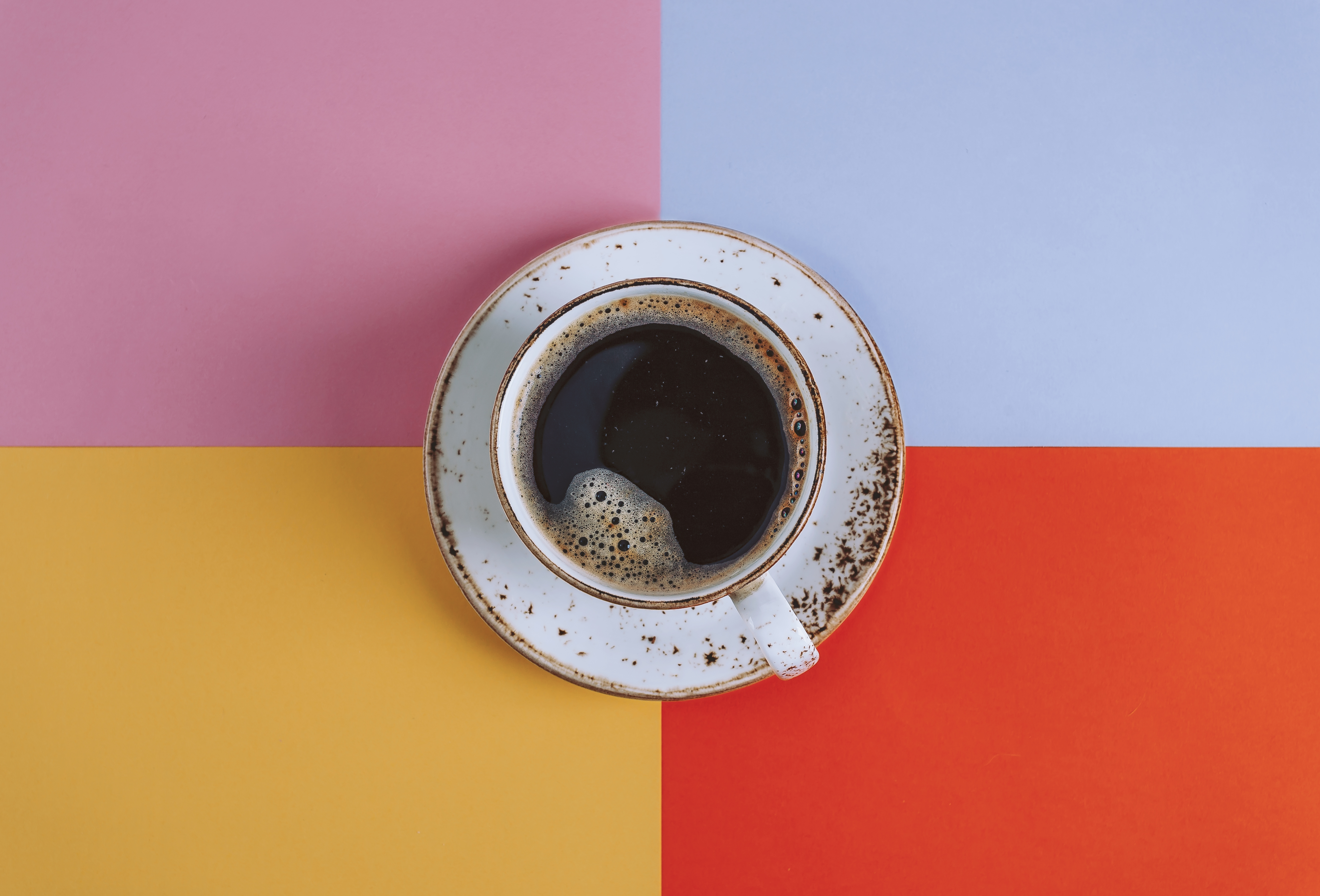 A cup of coffee against a multi-colored background.