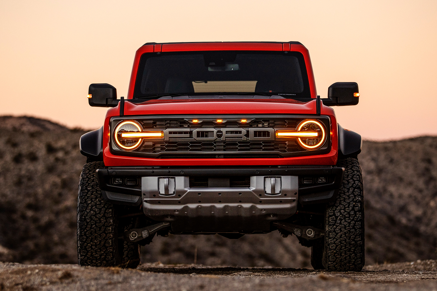 An off-road Ford Bronco Raptor with its headlights on shown from the front