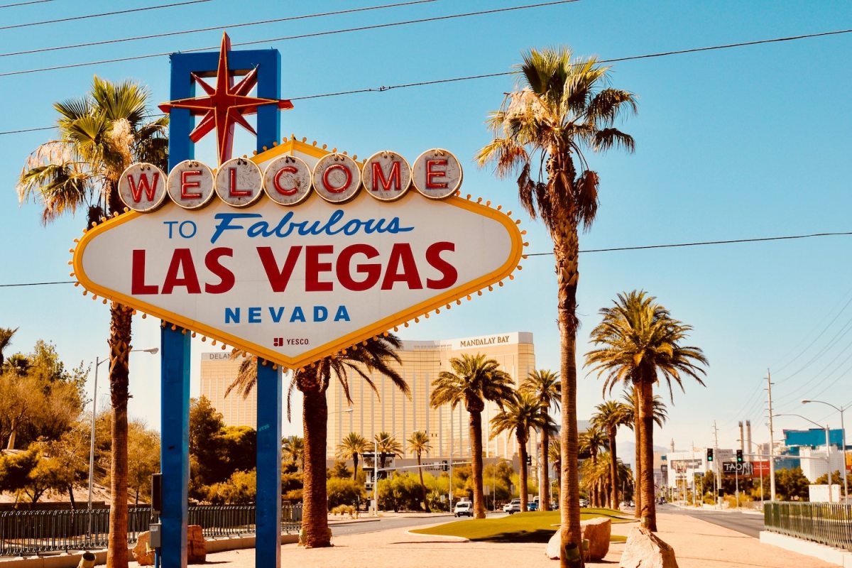 The famous "Welcome to Las Vegas" sign stands between palm trees under a cloudless sky