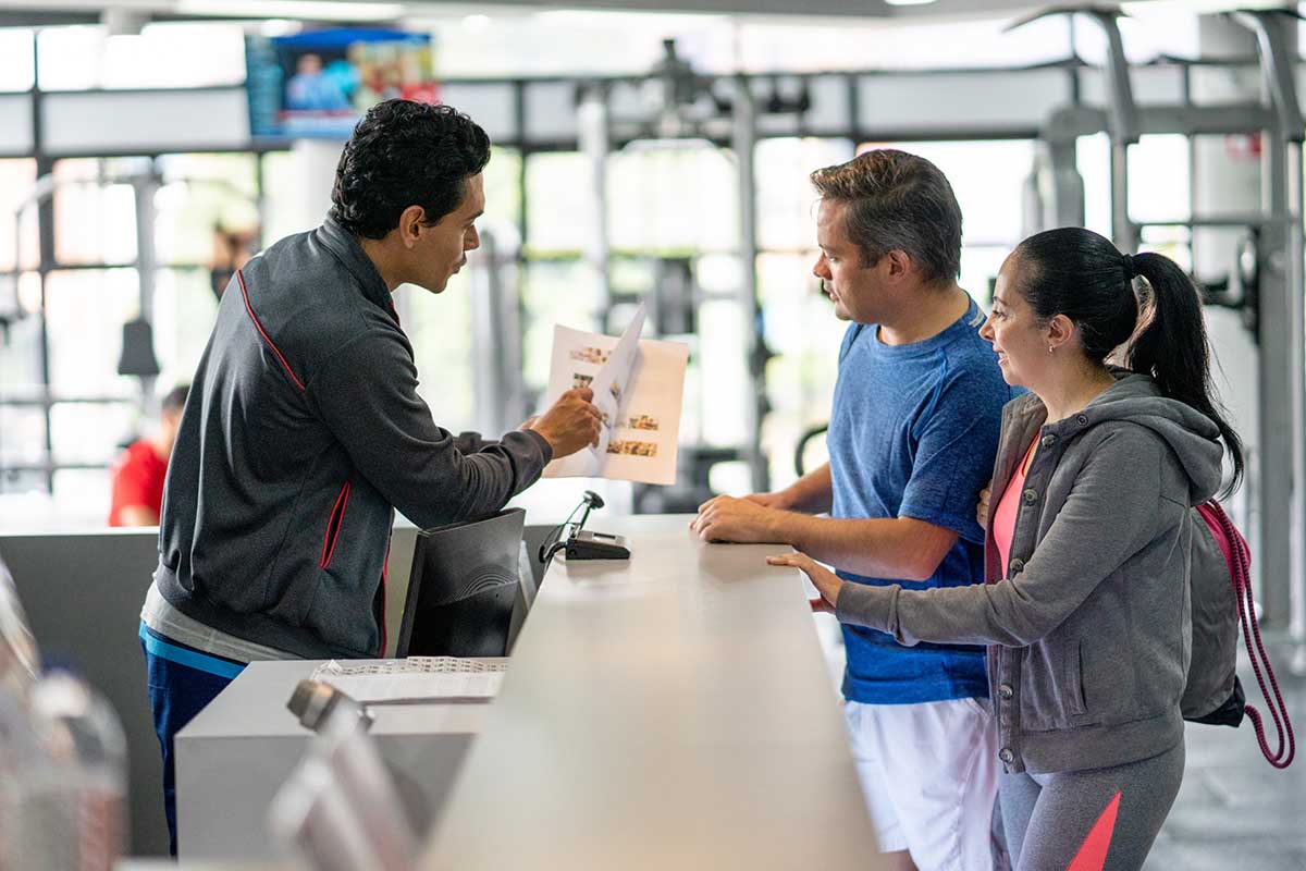 A couple registering at the gym with an employee showing off a catalog. The FTC wants to make it easier to cancel things like gym memberships.