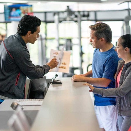 A couple registering at the gym with an employee showing off a catalog. The FTC wants to make it easier to cancel things like gym memberships.