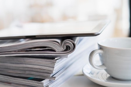Close up of coffee cup and digital tablet on top of magazine stack - stock photo. Amazon has announced it is ending magazine subscriptions, both for print and digital.