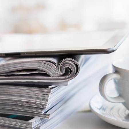 Close up of coffee cup and digital tablet on top of magazine stack - stock photo. Amazon has announced it is ending magazine subscriptions, both for print and digital.