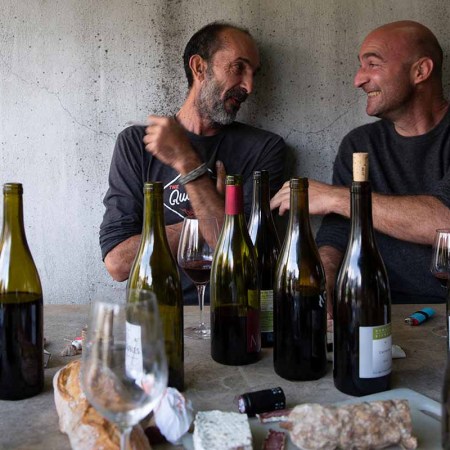 Two winemakers sitting at a table enjoying several bottles of natural wine. A new book goes explores and explains the world of natural wine.