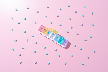 Heap of Blue Capsules in Pill Organizer on Pink Colored Background Directly Above View.