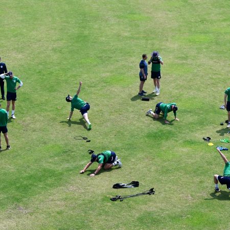 A bunch of cricket players stretching in the sun, from an aerial view.