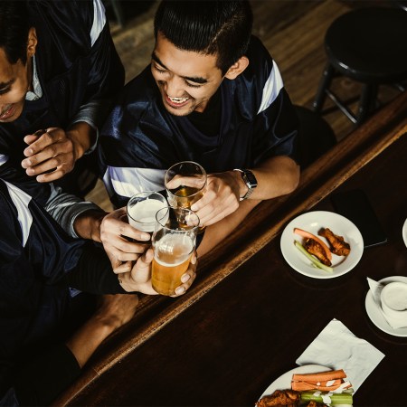 High angle view of excited sports fans toasting beer glasses at counter in bar