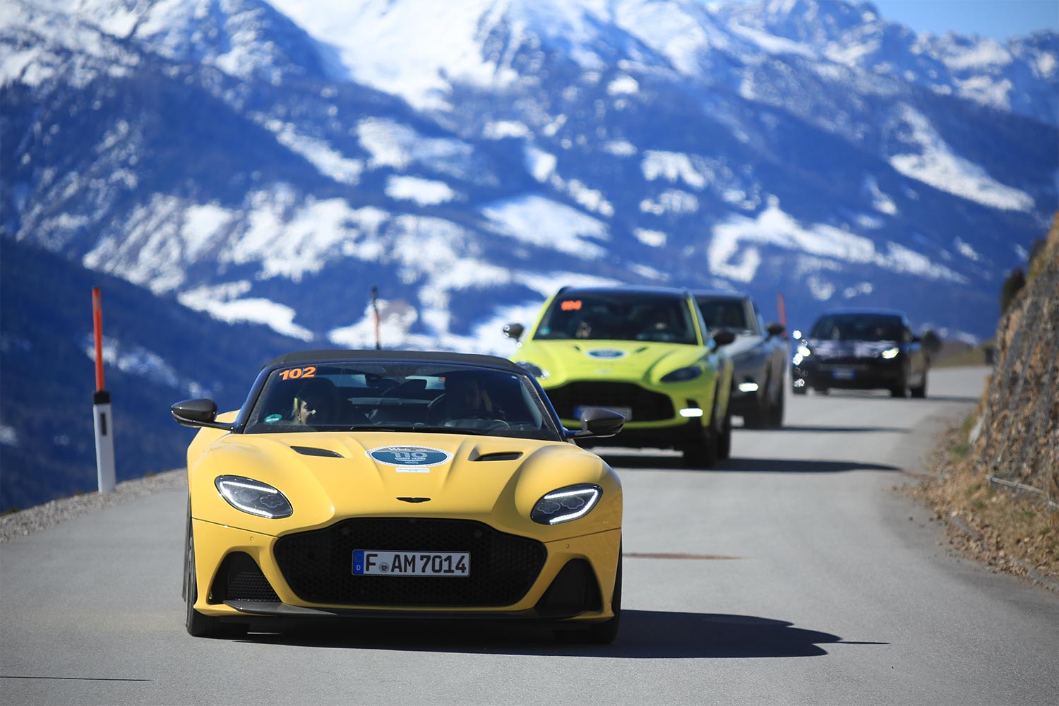 A line of modern supercars and SUVs drive through the mountains during Winterace 2023