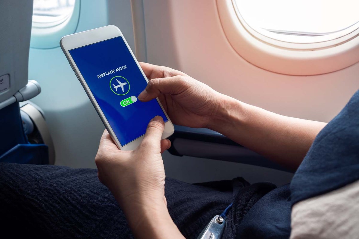 A person holding white smartphone turning on airplane mode. Is the phone setting really necessary during flight?