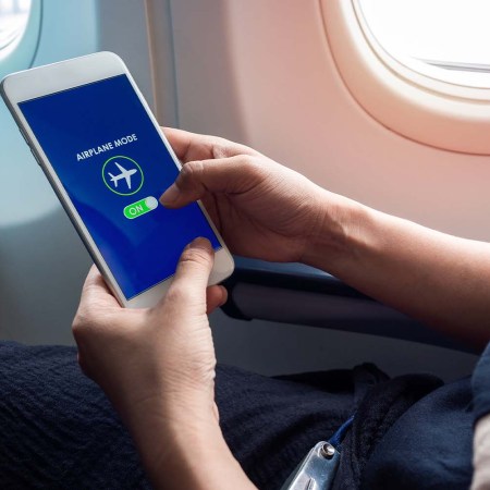 A person holding white smartphone turning on airplane mode. Is the phone setting really necessary during flight?