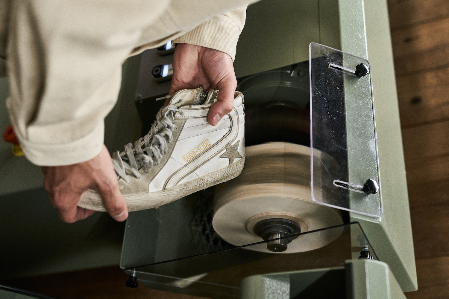 a man fixing a pair of white golden goose sneakers on a cobbler's wheel