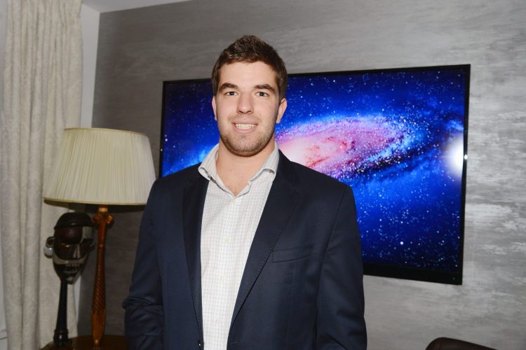 Wide shot of Billy McFarland standing in front of a television screen.