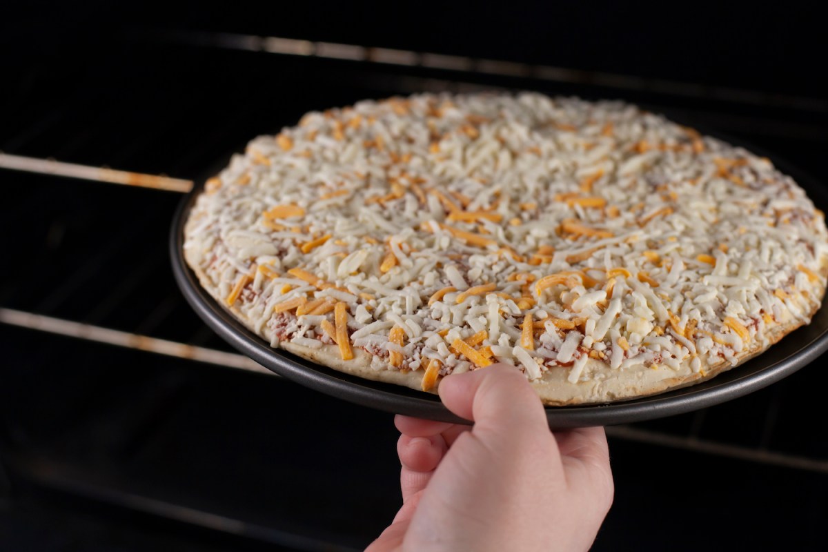 Putting a frozen cheese pizza into the oven to bake