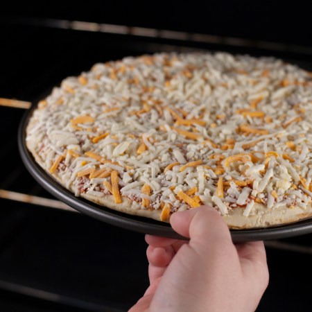 Putting a frozen cheese pizza into the oven to bake