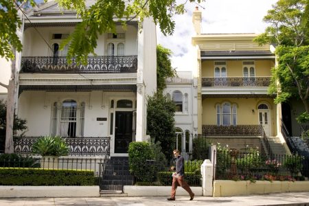 A row of townhouses on a sunny day with a pedestrian walking in front of them.