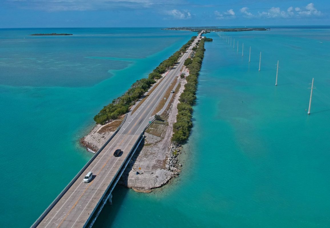 Highway going across small strip of land on top of large blue body of water.