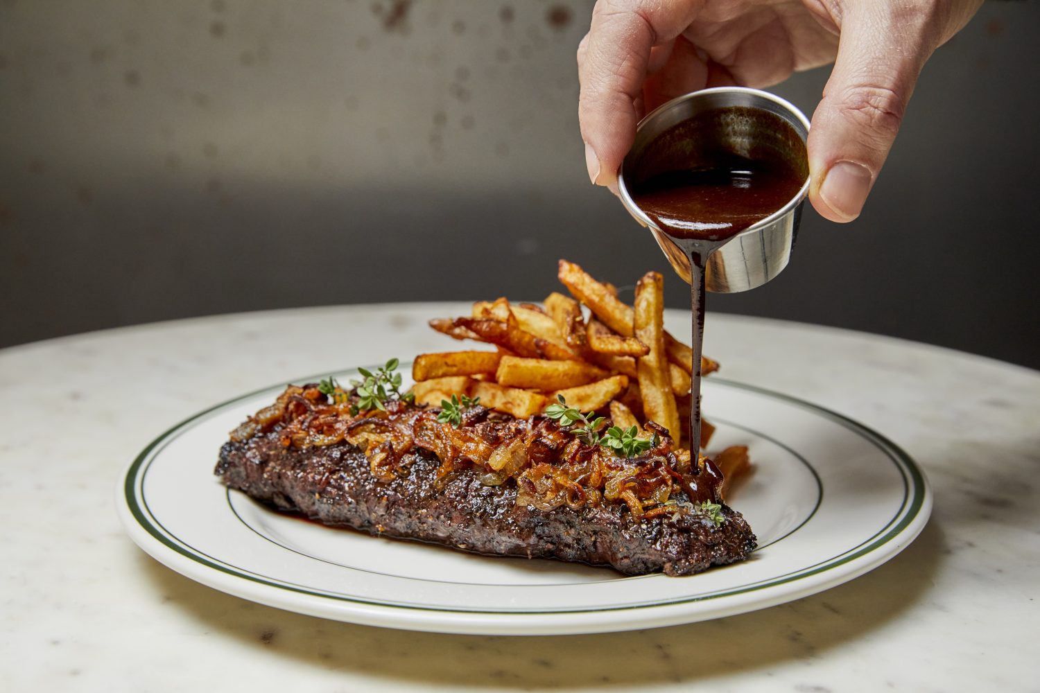 Steak and fries on a plate while sauce is poured on top of it.