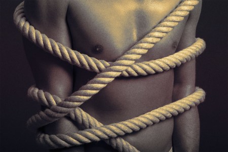 shirtless man tied up with a thick rope
