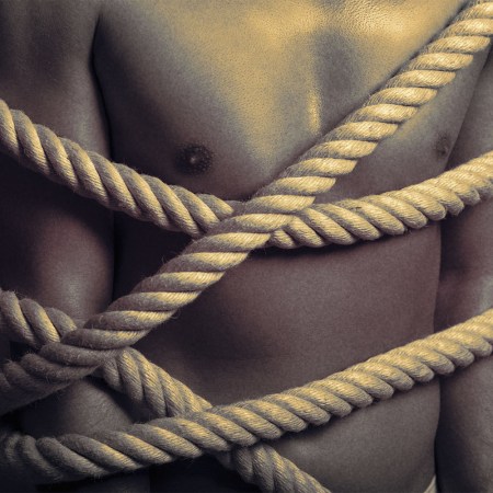 shirtless man tied up with a thick rope