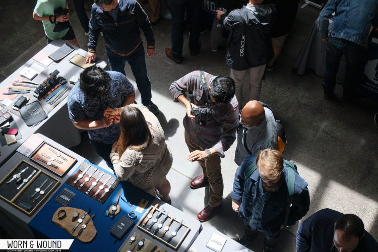 Overhead view of people looking at tables of watches.