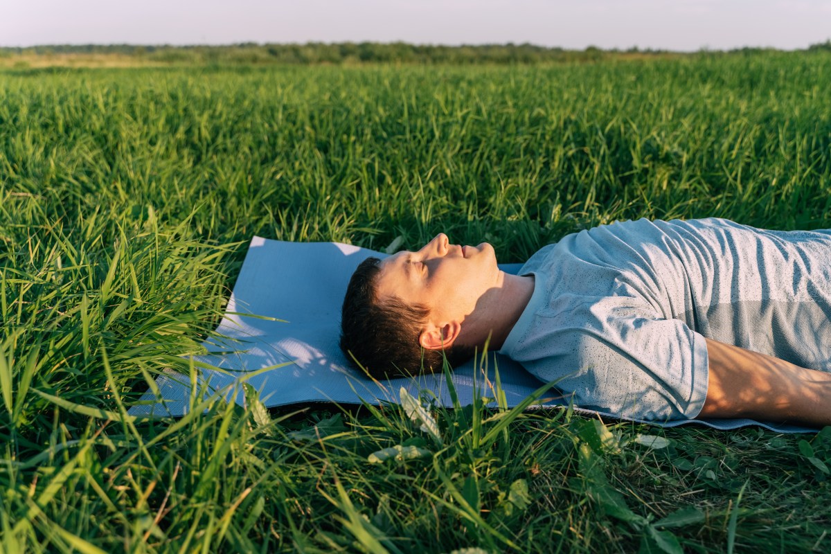 A man laying in a field breathing through his nose.