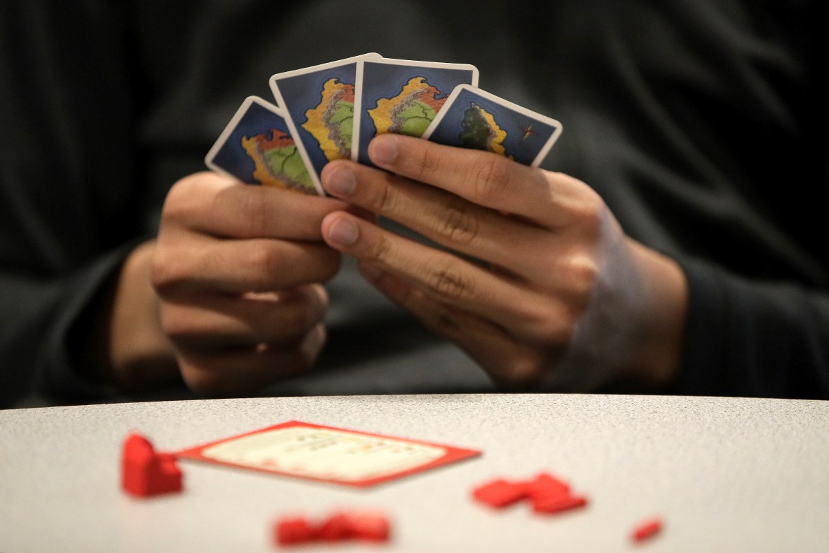 A man holding Catan playing cards in his hands. Here's why you should play Klaus Teuber's game for your health.
