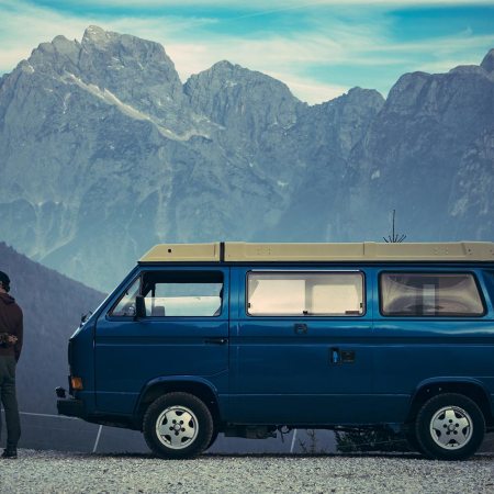 A man and a woman stand next to a camper van with mountains in the background