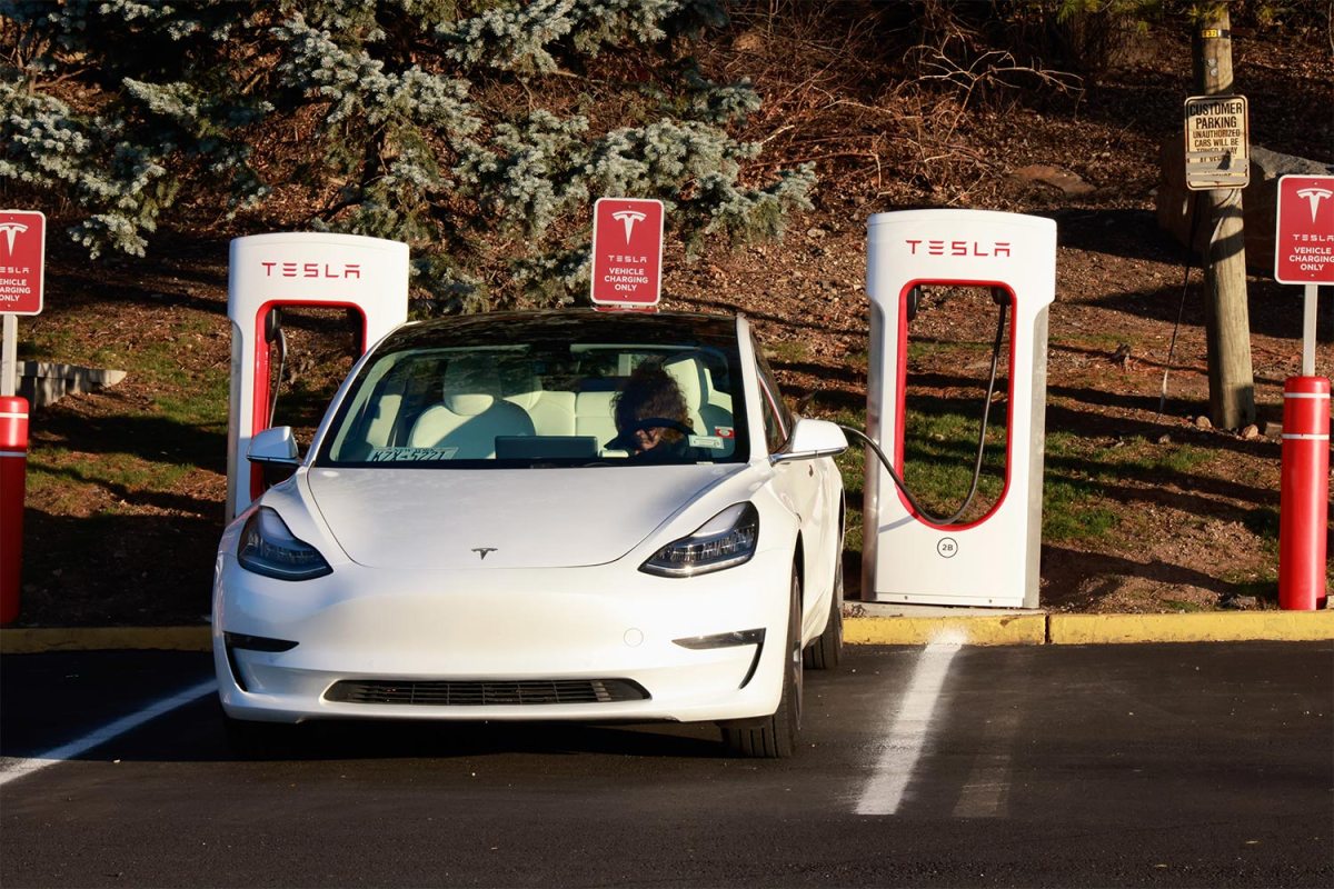 A person sitting in a Tesla EV at a charging station. According to reporting from Reuters, Tesla employees inappropriately shared images and videos recording by Tesla cars in an internal messaging system.