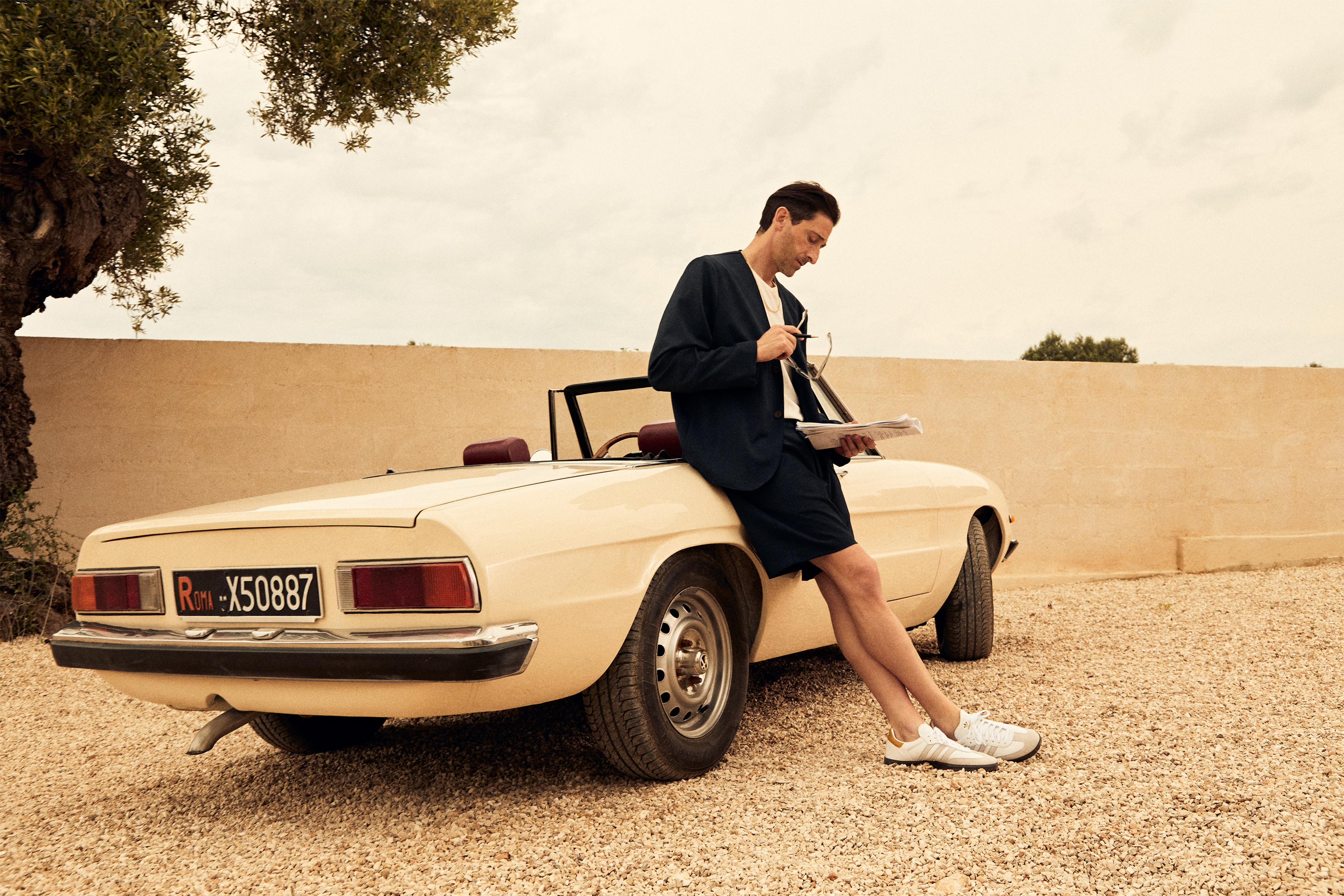 Adrian Brody leaning against a car in Kith clothing