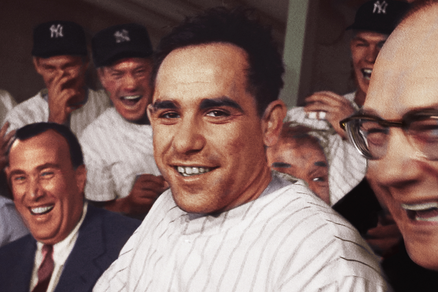 Yogi Berra in his Yankees uniform surrounded by laughing teammates and dapper men in suits during Mr. Berra's playing days