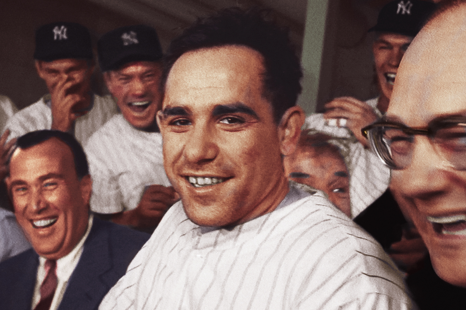 Yogi Berra in his Yankees uniform surrounded by laughing teammates and dapper men in suits during Mr. Berra's playing days