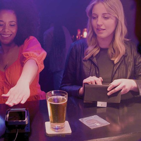 Two young women at a bar using Amazon's palm-scanning tech Amazon One to verify age and buy drinks