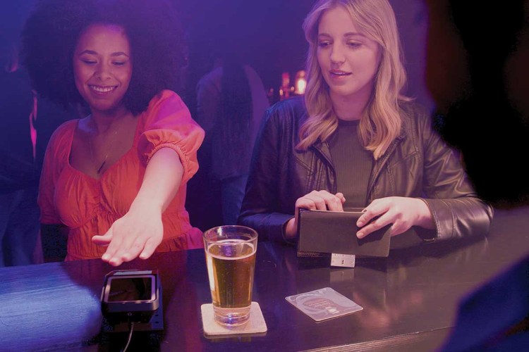Two young women at a bar using Amazon's palm-scanning tech Amazon One to verify age and buy drinks