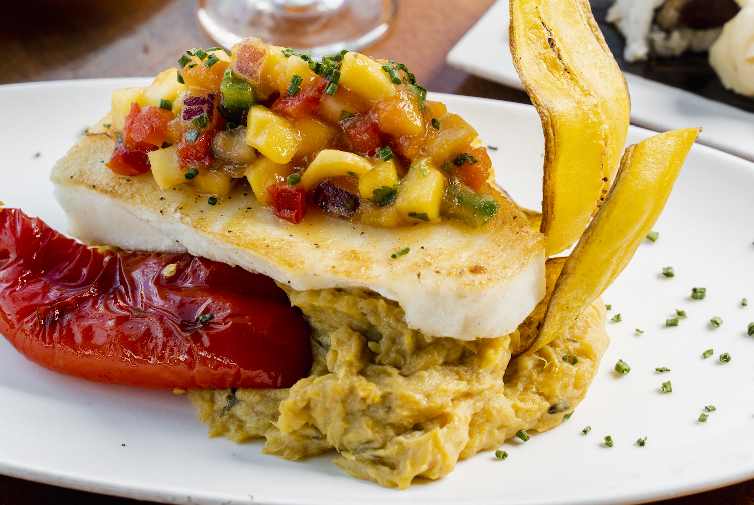a plated fish with plantain mash and grilled anaheim pepper.