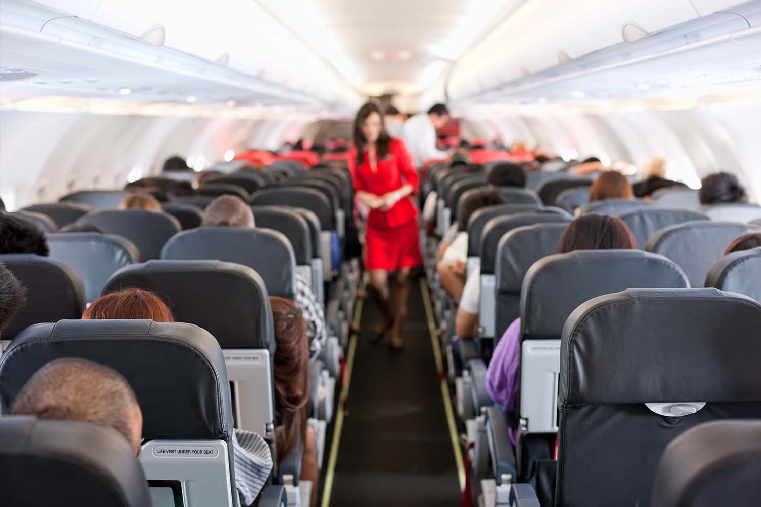 A flight attendant in the middle of an aisle on an airplane. Here's why flight attendants won't help you with your carry-on bags.