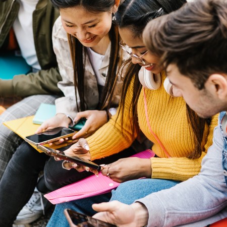 Diverse young teenage students having fun using mobile phone in college campus