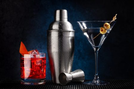 Cocktail shaker, negroni and martini cocktails on dark background