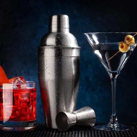 Cocktail shaker, negroni and martini cocktails on dark background