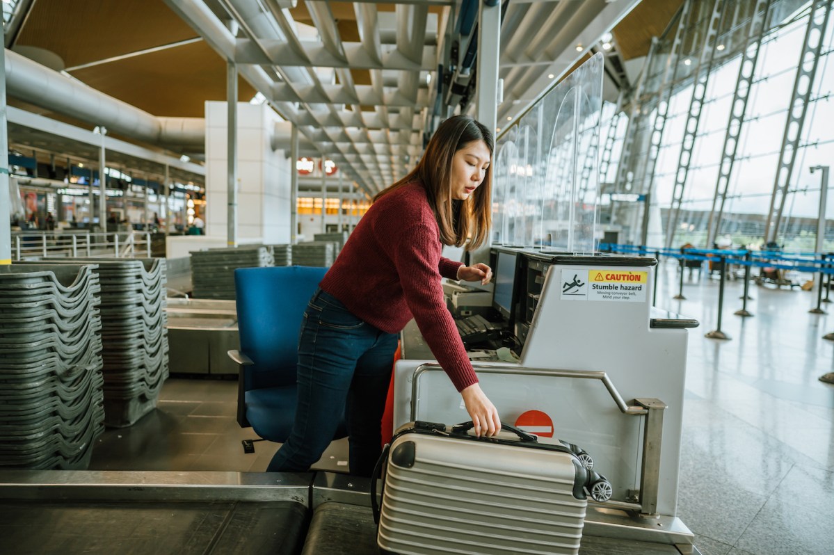Young female airline check-in assistant putting luggage on the scales at check-in counter in airport
