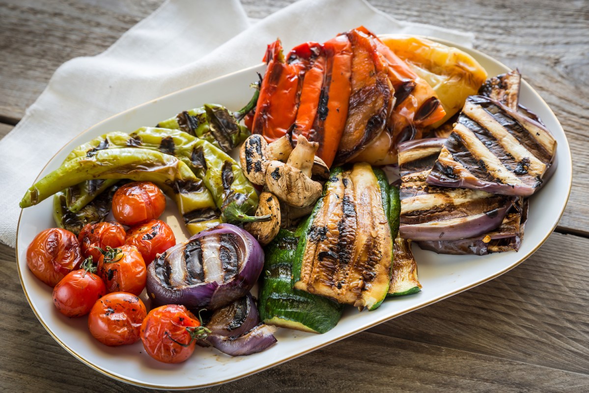 a white platter filled with grilled vegetables, including nightshades, on a wooden table