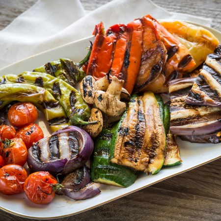 a white platter filled with grilled vegetables, including nightshades, on a wooden table