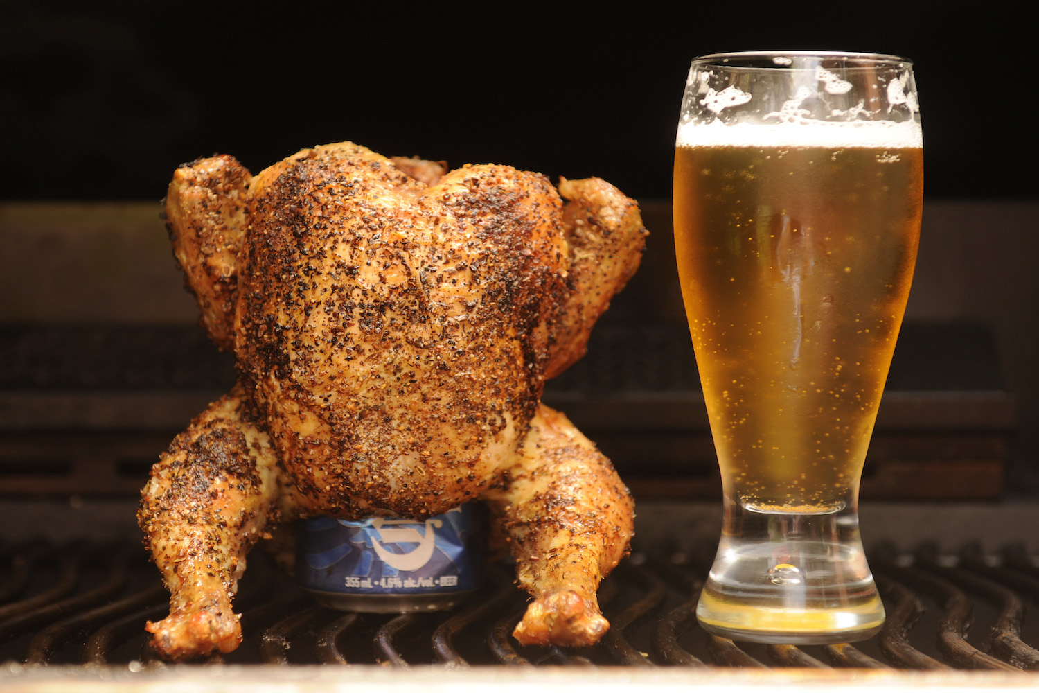a full cooked chicken with a beer can inside of it and standing upright next to a glass of beer