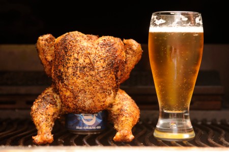 a full cooked chicken with a beer can inside of it and standing upright next to a glass of beer