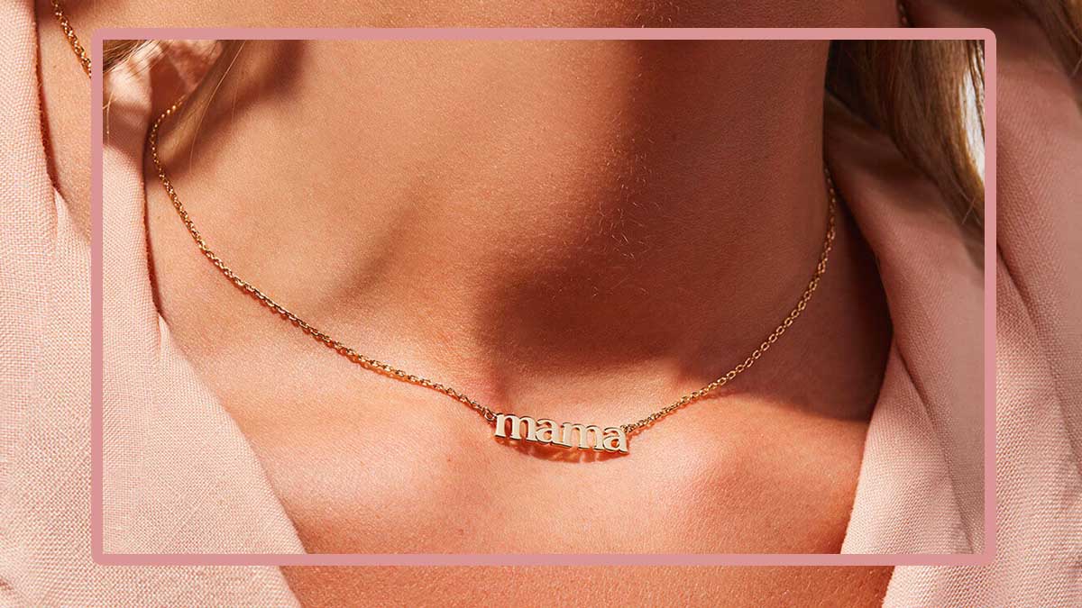 A woman wearing a necklace that spells "mama," a great piece o jewelry to gift this Mother's Day